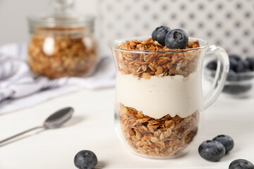 Tasty yogurt with muesli and blueberries in cup served on white wooden table
