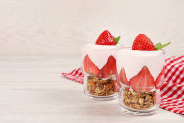 Glasses of tasty yogurt with muesli and strawberries served on white wooden table, space for text