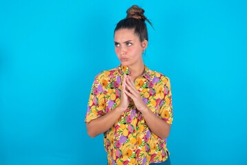beautiful brunette woman wearing colourful shirt over blue background steepled fingers and looks...