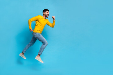 Fototapeta na wymiar Full size profile portrait of sporty cheerful man run jump look empty space isolated on blue color background