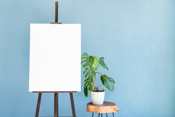 Wooden easel with blank canvas on light blue background for mockup design