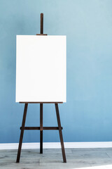 Wooden easel with blank canvas on light blue background for mockup design
