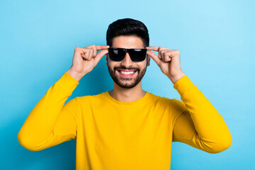 Photo of attractive confident guy dressed yellow pullover arms dark eyewear smiling isolated blue color background