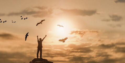 silhouette Man rising hands with eagles flying on the top of a mountain during sunset time. outdoor...