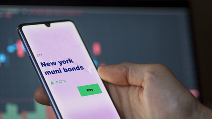 An investor's analyzing the NY municipal bond on screen. A phone shows the ETF's prices new york muni bonds