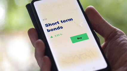 An investor's analyzing the short-term fund bond on screen. A phone shows the ETF's prices short term bonds