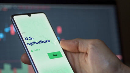 An investor's analyzing the u.s., u.s.a. etf fund on screen. A phone shows the ETF's prices U.S. agriculture to invest