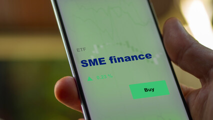 An investor's analyzing the SME finance etf fund on screen. A phone shows the small and medium-sized enterprises ETF's prices stocks to invest