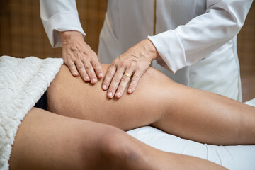 Fototapeta na wymiar Um profissional fazendo massagem terapeutica na perna do paciente que está deitado na maca.