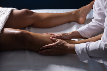 Um profissional fazendo massagem terapeutica na perna do paciente que está deitado na maca. - obrazy, fototapety, plakaty