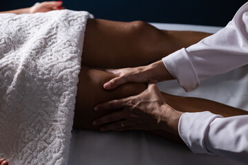 Um profissional fazendo massagem terapeutica na perna do paciente que está deitado na maca.