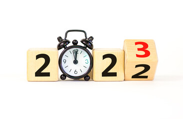 Business concept of 2023 new year symbol. Turned a wooden cube and changed number 2022 to 2023. Black alarm clock. Beautiful white table white background, copy space. Business 2023 new year concept.