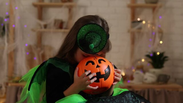 charming little girl in a green Halloween costume of a witch or sorceress with a pumpkin lantern jack, a basket for sweets in her hands. autumn concept