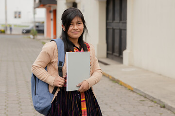 Hispanic young woman with notebook and backpack outside school in rural area - Mayan woman ready to go to study - Latina student in the city