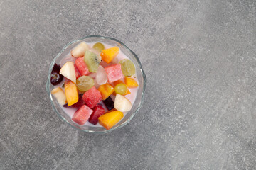 Es Buah or Es Campur on grey background, top view. Popular indonesian fruits cocktail dessert. Fruit soup with yogurt and shaved ice