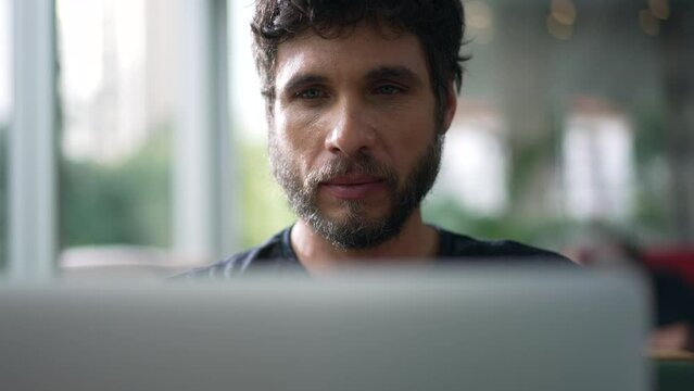 Man staring at laptop screen seated at coffee shop. Person looking at computer with serious expression browsing internet online