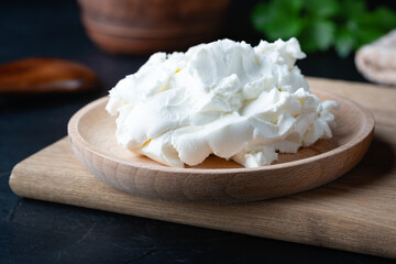 Cottage cheese on a wooden stand. Cottage cheese in a bowl. Soft cheese and wooden spoon on a wooden boards