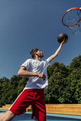 low angle view of man in sportswear throwing ball into basketball hoop