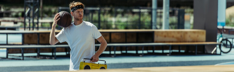 young basketball player with ball and record player walking near stadium, banner