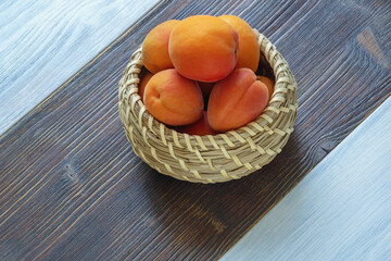 Ripe apricots in small basket on rustic table. Copy space