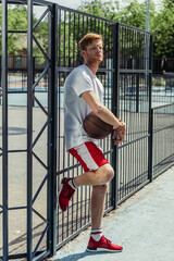 full length of man in sportswear standing with ball near fence of stadium