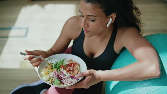 Video of sporty young woman eating healthy while listening to music sitting on the floor at home.