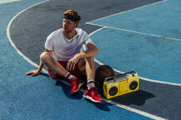 basketball player in red sneakers and bandana sitting on court near boombox