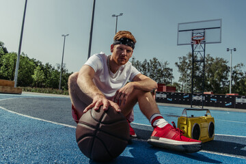 basketball player in sportswear and bandana sitting on court with ball and tape recorder