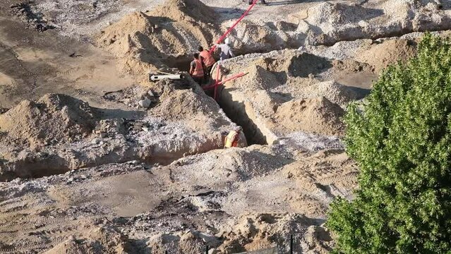Workers lay pipes in a trench for electrical cables