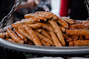 Close up: process of grilling fresh meat sausages on big round hanging grill at summer local food market. Outdoor cooking, barbecue, gastronomy, cookery, street food concept