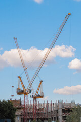 Yellow tower cranes and unfinished building construction against summer cloudy blue sky. Building process, architecture, urban, engineering, industrial and development concept