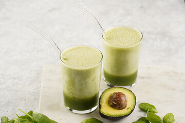 A glass of green healthy detox smoothie with spinach, matcha powder and a glass straw, fresh...