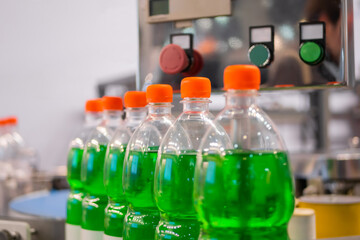 Row of pet bottles with green lemonade and orange caps on conveyor belt of automatic liquid filling machine at plastic exhibition - close up. Manufacturing, industry and technology equipment concept - Powered by Adobe