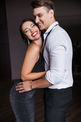 Cheerful woman in dress hugging boyfriend at home