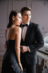 Elegant man in formal wear hugging seductive girlfriend at home