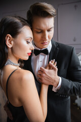 Naklejka premium Man in suit touching hand of elegant girlfriend at home