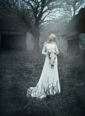 A creepy woman in a white dress with a canvas bag on her head, with a cow's skull in her hands....