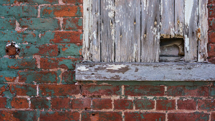 Red brick and peeled paint wall with old wooden window and rusty nails