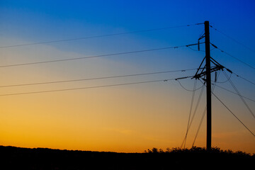 A tower with power lines from a nuclear power plant in Ukraine against the background of a sunset with the colors of the flag of Ukraine