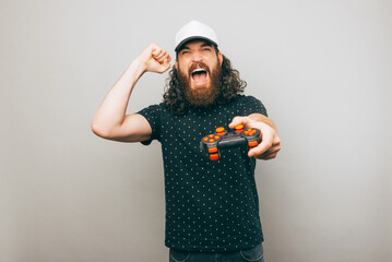 Excited gamer is holding his console and celebrating his win over a gray wall © Vulp