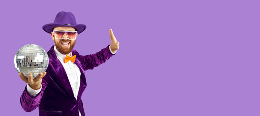 Banner narrow shot of smiling party man in jacket and hat isolated on purple studio background hold glitter disco ball. Happy male performer or entertainer have fun enjoy celebration. Entertainment.