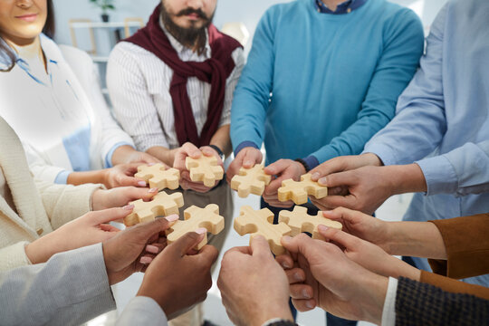 Close up of diverse businesspeople connect jigsaw puzzle pieces search business solution together. Employees or colleagues engaged in teambuilding training. Teamwork and cooperation.