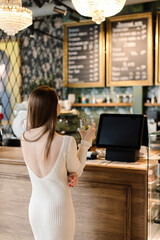 Fototapeta na wymiar A young woman stands at the cash register and reads the menu, makes a choice. Back view. High quality photo