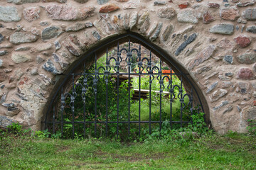A hole in a fortified stone wall closed with a metal forged grating - castle back door