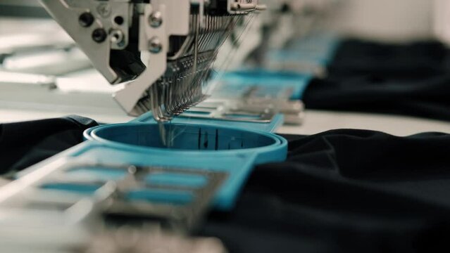 Close up of automated sewing machines stitching quickly black cotton shirts at a production line of sports clothing and equipment factory