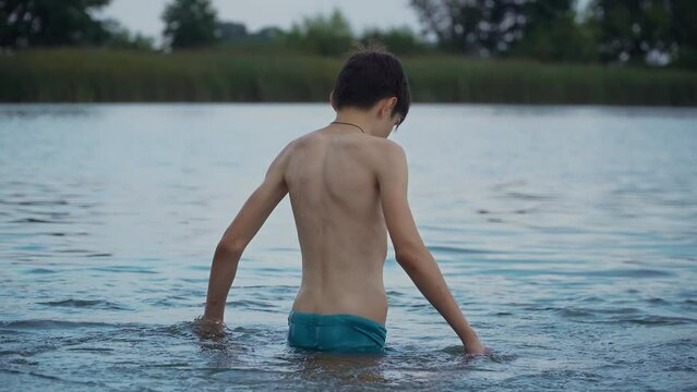 Young boy teenager in lake splashing and making waves in water at evening. Active lifestyle and traveling in holiday concept
