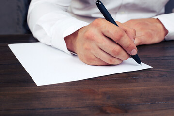 A man's hand writes on a blank sheet in a notebook.