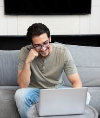 Smiling handsome man sitting on the couch and working on laptop at home. Online education and distant work concept