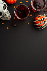 Halloween party concept. Top view vertical photo of drink in glasses with floating spiders straws cockroach skull skeleton hand holding pumpkin and confetti on isolated black background with copyspace