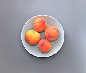 four juicy ripe peaches in a plate on a gray background
